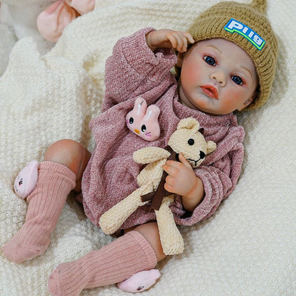 Close-up of the reborn baby doll with a teddy bear and pink rabbit toy.