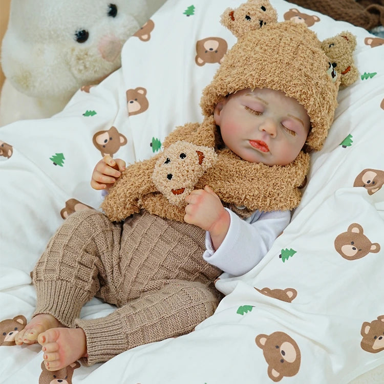 Reborn baby doll lying on a bear-themed blanket with a plush teddy bear.