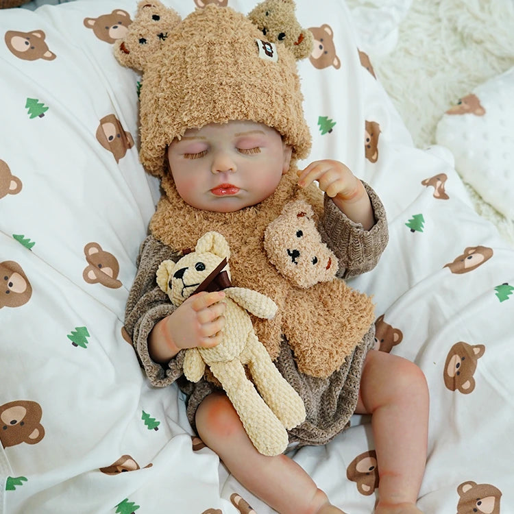 Reborn baby doll wearing a cozy bear outfit, holding a teddy bear.