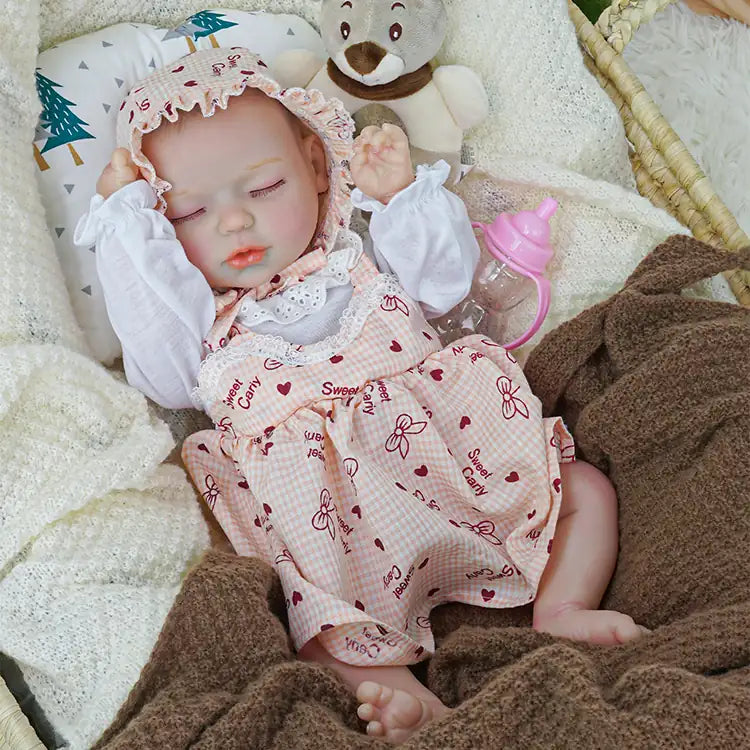 Realistic reborn doll with a pacifier, dressed in a pink checkered dress and white blouse, sleeping in a wicker basket with a teddy bear and covered by cozy blankets, evoking a peaceful scene.