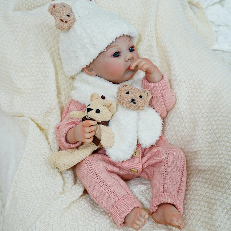 Reborn baby doll snuggled in a soft blanket, clutching a teddy bear.