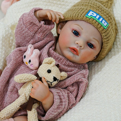 Reborn baby doll with a teddy bear, resting on a soft blanket.