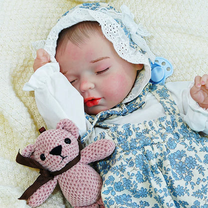 Reborn baby doll in a blue floral dress with a bonnet, peacefully sleeping while holding a pink stuffed toy.