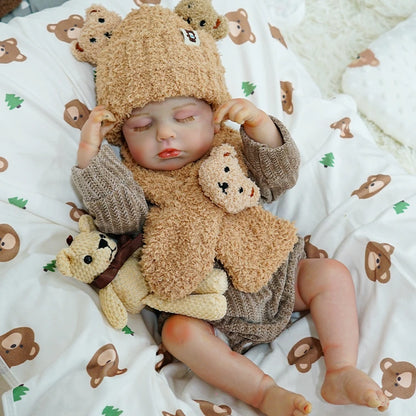 Reborn baby doll gently holding its teddy bear, eyes closed in peaceful sleep.