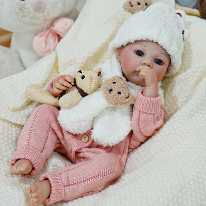 Reborn baby doll lying down with a pacifier, holding a teddy bear.