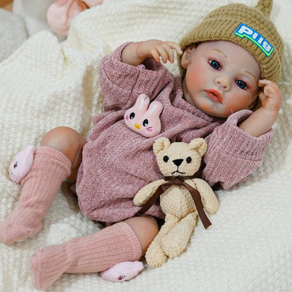 Reborn baby doll lying down in a cozy outfit, clutching a teddy bear.