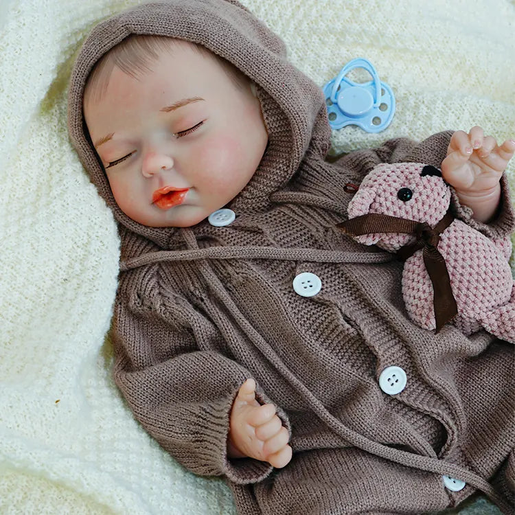 A reborn baby doll lying on its side, eyes closed, wearing a hooded outfit.