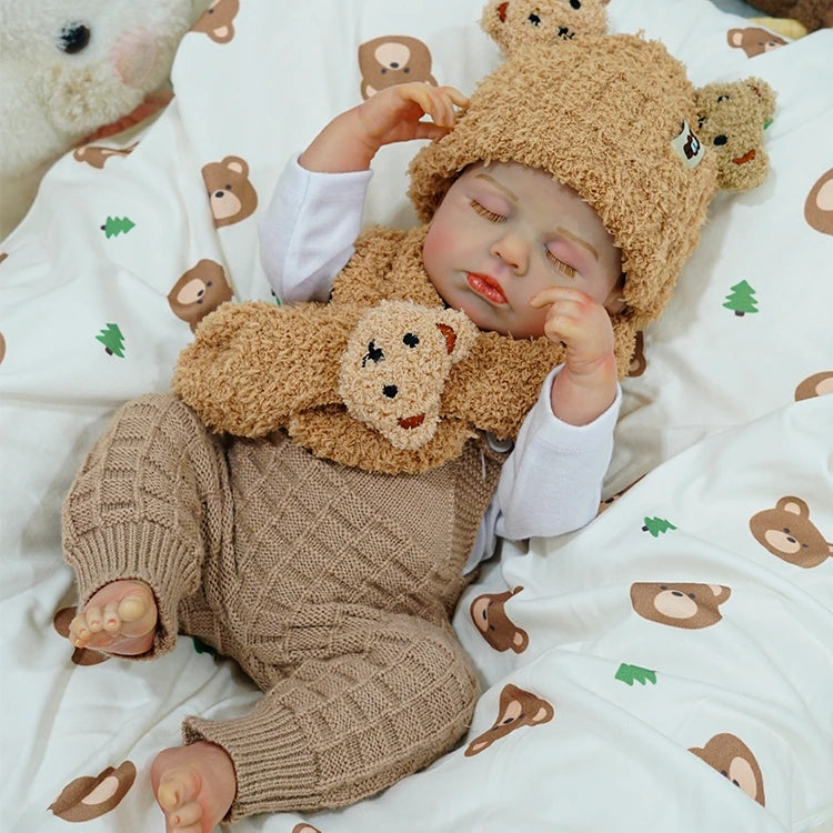 Reborn baby doll in a cozy outfit, lying with a teddy bear.