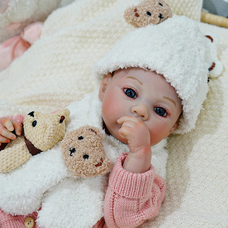 Close-up of reborn baby doll sucking on a pacifier, dressed in a bear-themed outfit.