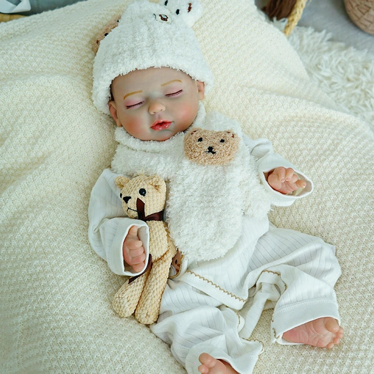 Reborn baby doll cuddling a teddy bear with soft blanket.