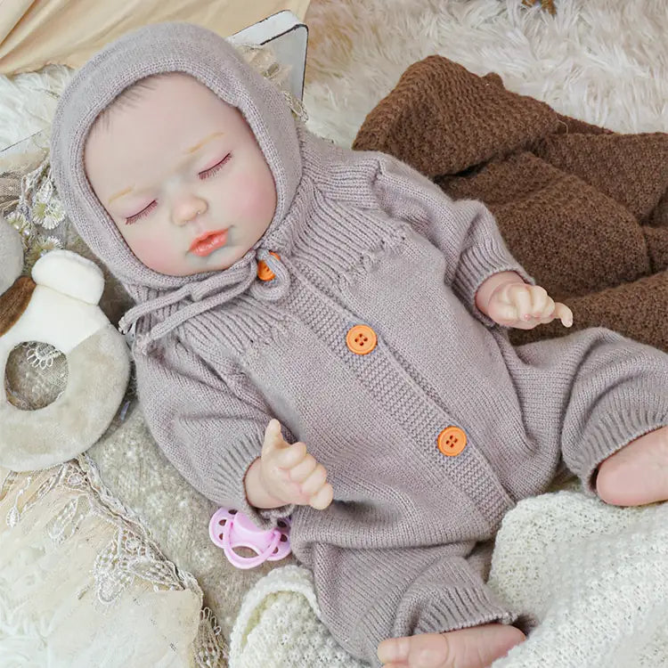 A close-up view of a reborn doll in a lavender outfit, sleeping under a lace canopy. A pink pacifier is in its mouth.
