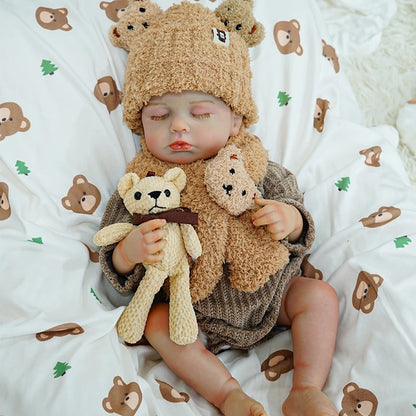 Reborn baby doll relaxing with a teddy bear, lying on a bear-patterned blanket.