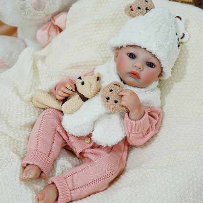 Reborn baby doll resting with a teddy bear on a cozy blanket.