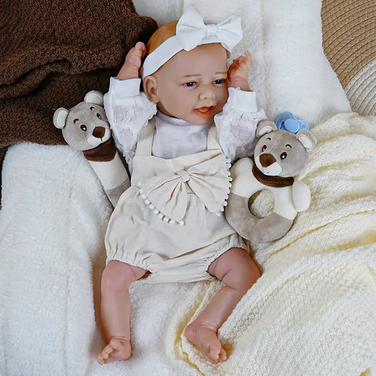 Happy reborn baby doll in pink pajamas with sea creatures, holding a dummy and a bottle, sitting on a white fluffy blanket.