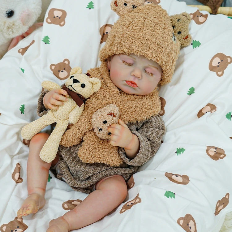 Reborn baby doll sitting with a teddy bear, wearing a knitted bear hat and scarf.