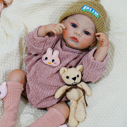 Close-up of the reborn baby doll with a teddy bear and pink rabbit toy.