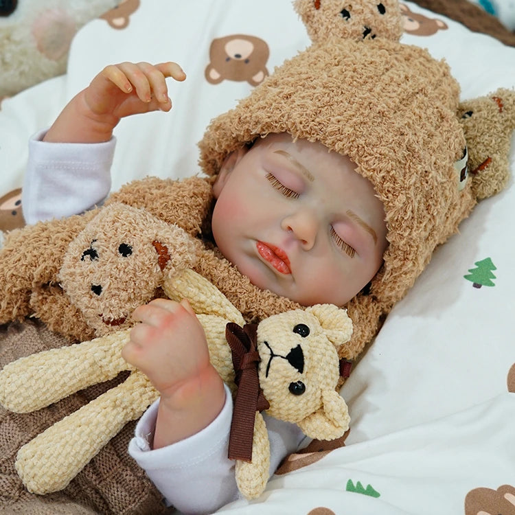 Reborn baby doll snuggling a teddy bear on a patterned blanket.