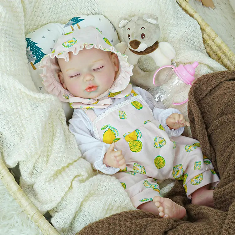 A serene reborn baby doll adorned in a pink outfit with lemon patterns and a matching bonnet, lying in a basket filled with soft blankets. The scene is completed with a plush teddy bear and a baby bottle, evoking a nurturing environment.