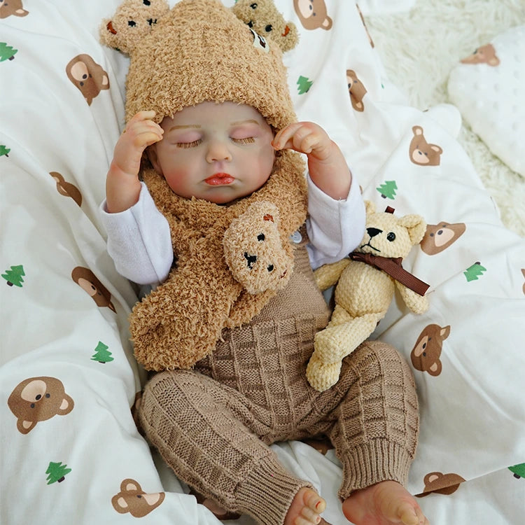 Reborn baby doll sleeping soundly with a small teddy bear.