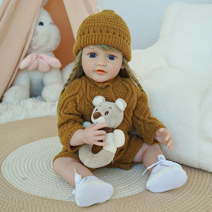 Reborn baby doll in brown knit outfit holding a teddy bear.