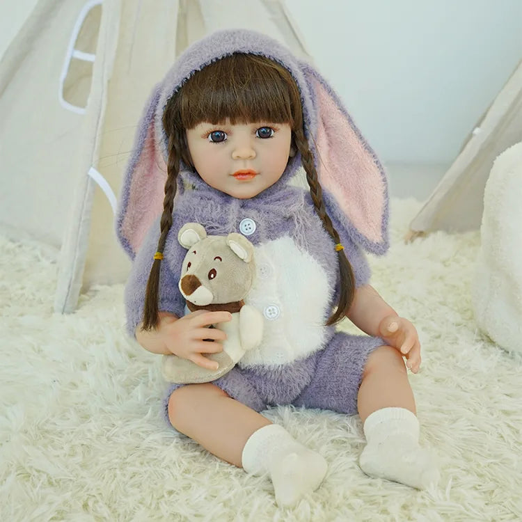 Reborn doll in purple bunny outfit, holding a teddy bear.
