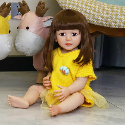 The toddler doll sitting on a colorful couch, legs crossed, still in the yellow dress, showing more of the background.