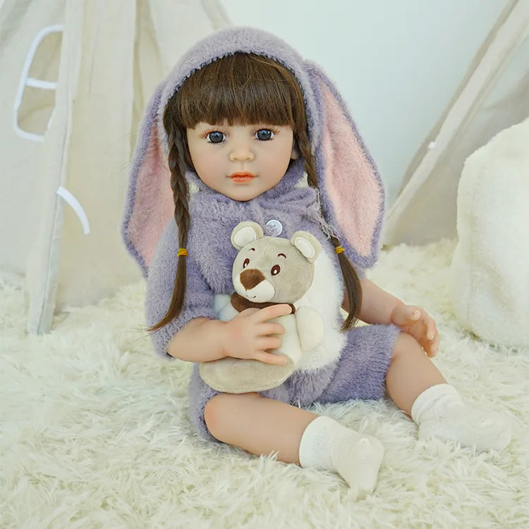 Reborn doll in purple bunny outfit, sitting with a teddy bear.