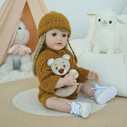 Reborn baby doll seated, wearing a brown knit outfit and hat, holding a teddy bear.