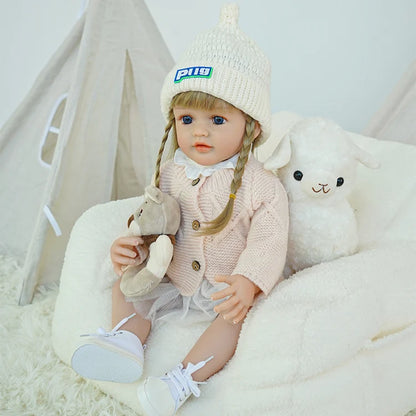 Reborn doll sitting on a chair with a toy lamb beside.