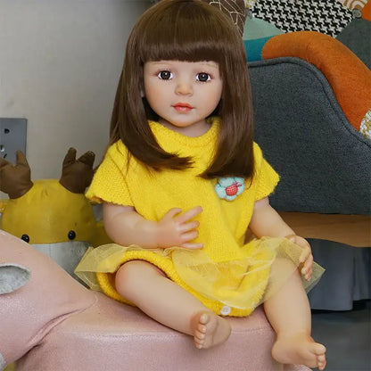 The toddler doll sitting on a pink chair, legs stretched out, looking directly at the camera, showing off the details of her yellow dress.