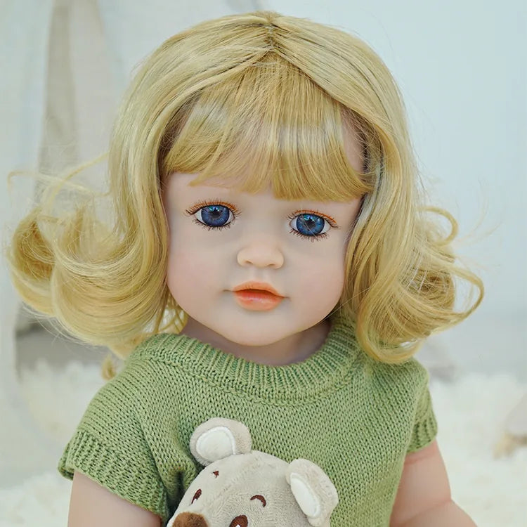 Reborn doll in green dress sitting on a carpet, with a toy lamb beside.