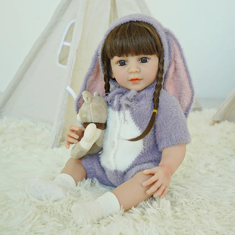 Reborn doll in purple bunny outfit, holding a teddy bear, sitting on the carpet.