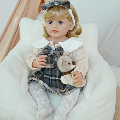 Reborn Toddler Doll sitting on a rug, holding the bear plush in her lap.