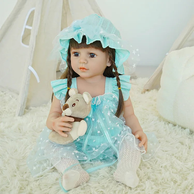 Charming toddler reborn doll in a blue starry dress and hat, holding a teddy bear, seated on a fluffy white carpet.