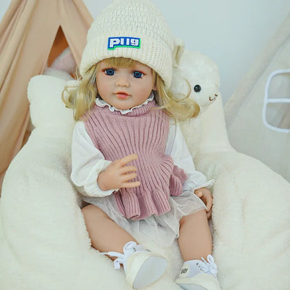 Reborn baby doll in pink knit dress with white shoes, holding a teddy bear.