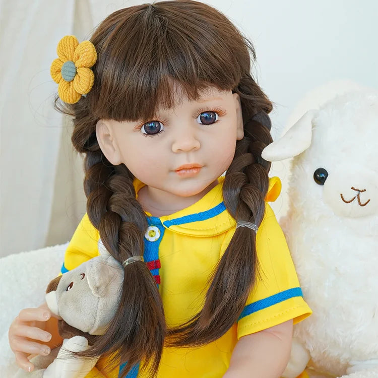 The reborn baby doll in a yellow dress, sitting on a soft chair, with a teddy bear and a plush sheep, displaying her sweet expression.