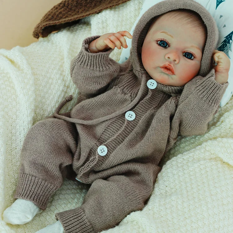 Reborn doll with hand raised, dressed in a cozy outfit.