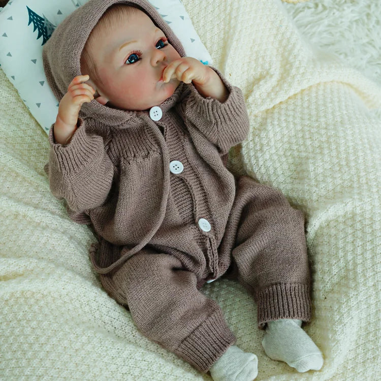 Reborn doll sitting up, looking serene in a knitted outfit.