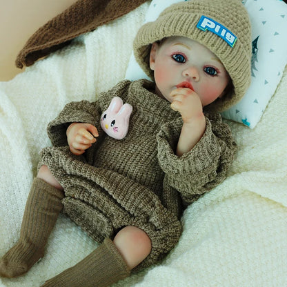 Lifelike reborn baby doll sitting with a plush bunny in a brown knit outfit.