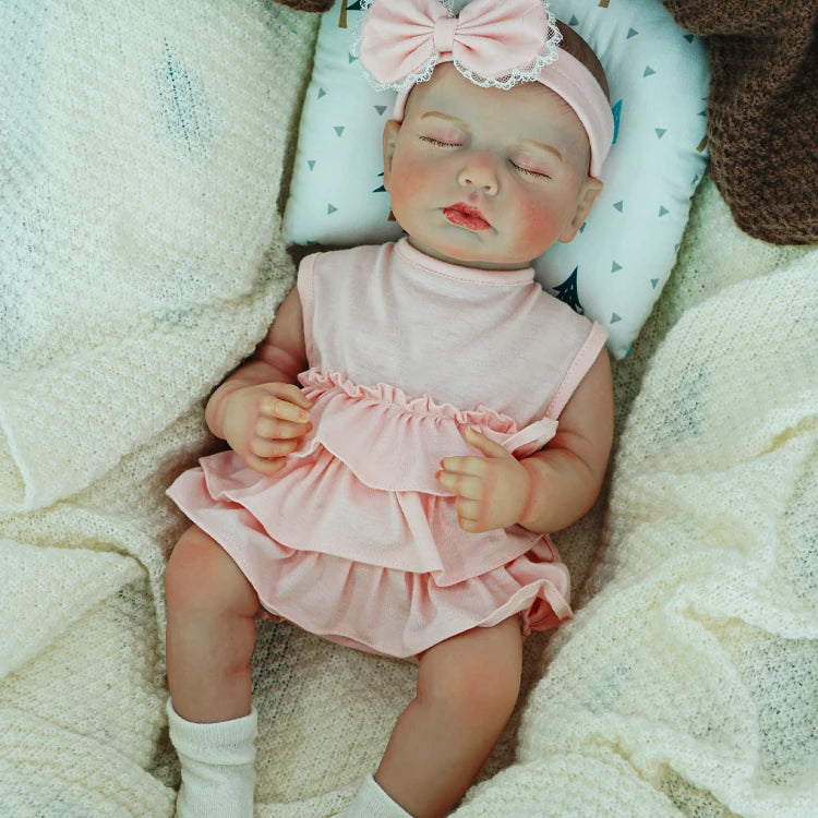 Reborn baby doll in a pink dress with a bow headband.