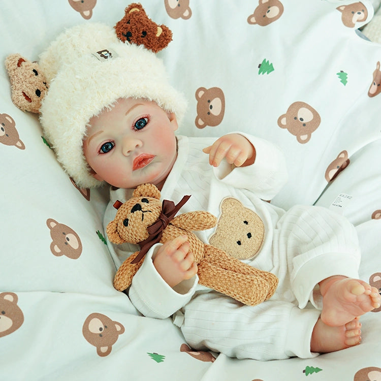 Reborn doll lying down, cuddling a teddy bear.