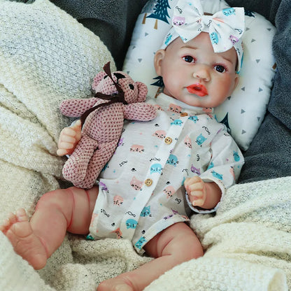 The reborn baby doll resting on a blanket, dressed in a patterned onesie and bow headband.