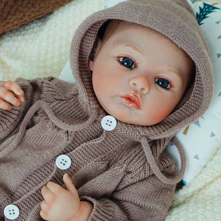 Lifelike reborn doll sitting in a cozy outfit