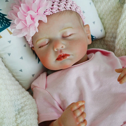 Reborn baby doll with pink flower headband, sleeping peacefully.