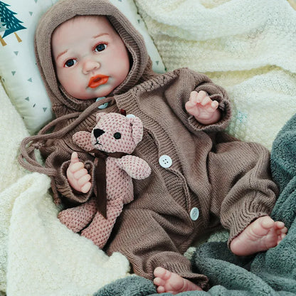 The reborn baby doll lying down, dressed in a cozy brown knit outfit, with a soft teddy bear, exuding warmth and comfort.