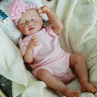 Reborn baby doll stretching arms in a pink onesie