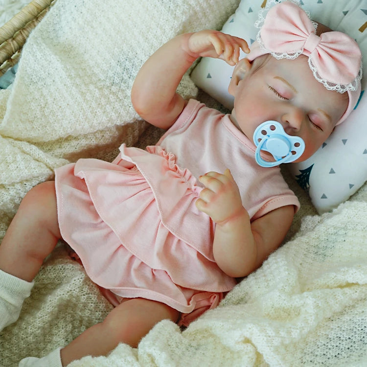 Reborn doll in a pink dress with a pacifier.