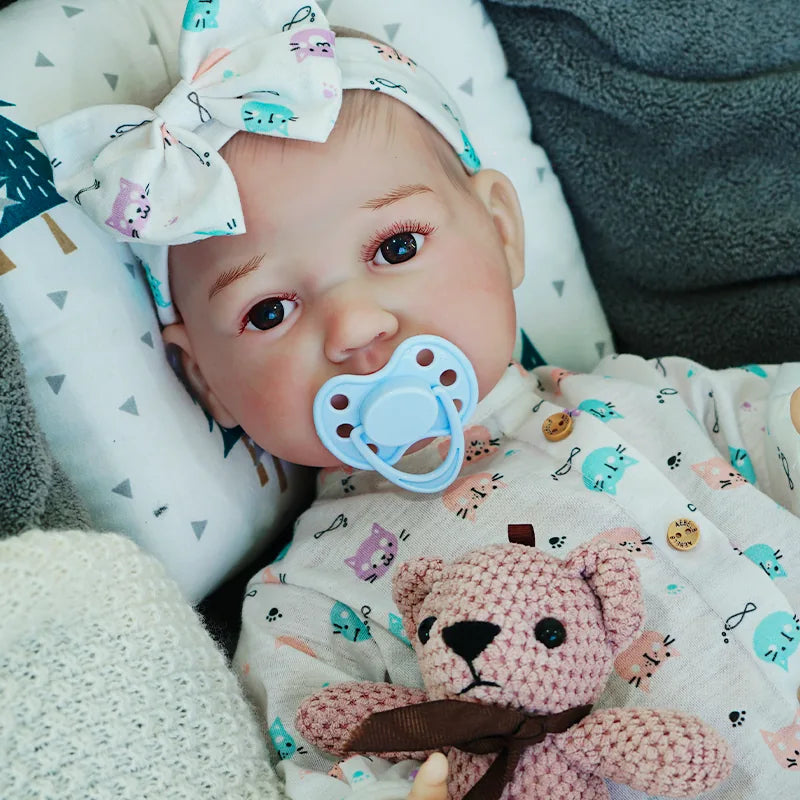 The reborn baby doll with a pacifier, dressed in a patterned onesie, lying on a soft blanket.