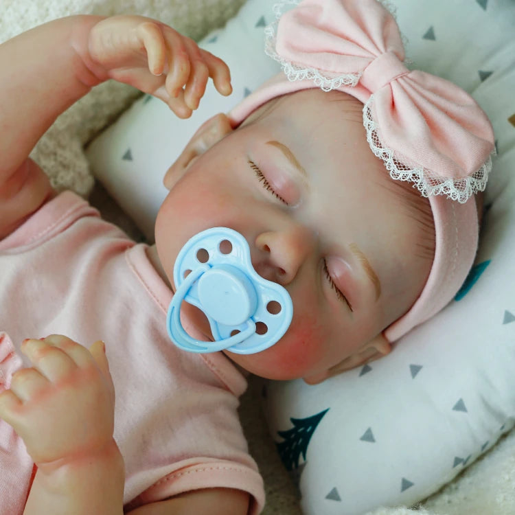 Sleeping reborn baby doll with a pacifier and bow.
