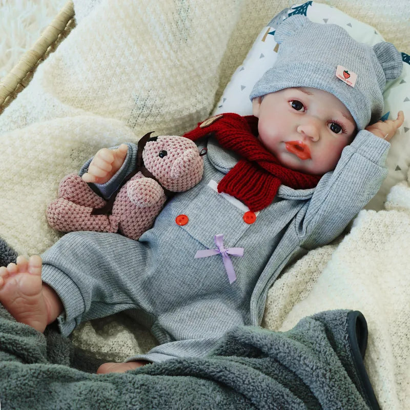 The reborn baby doll lying down with a relaxed expression, dressed in a gray outfit, and holding a soft teddy bear.